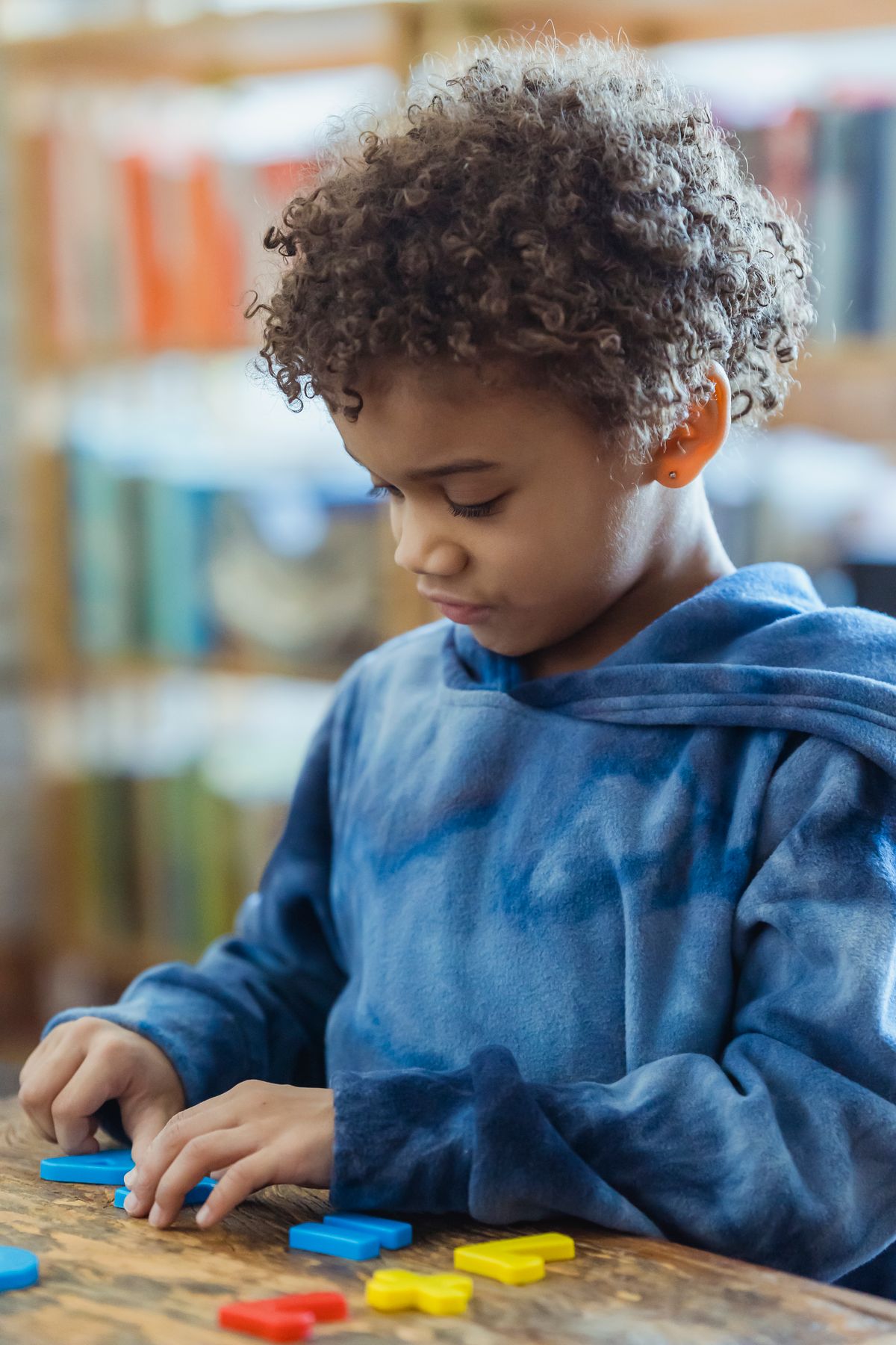 Un enfant concentré assemble des lettres sur une table.