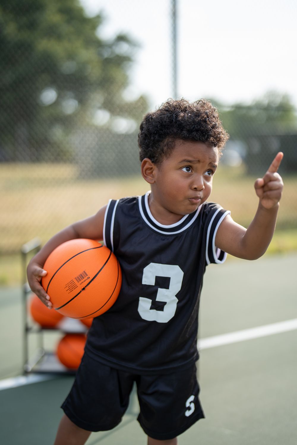 Un enfant, ballon de basket sous le bras, indique une direction du doigt.
