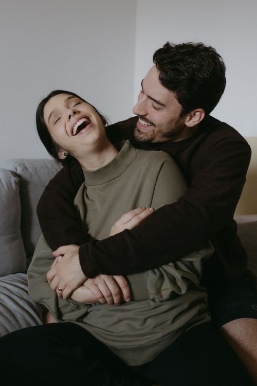 Un couple partage un éclat de rire en s’enlaçant sur un canapé.